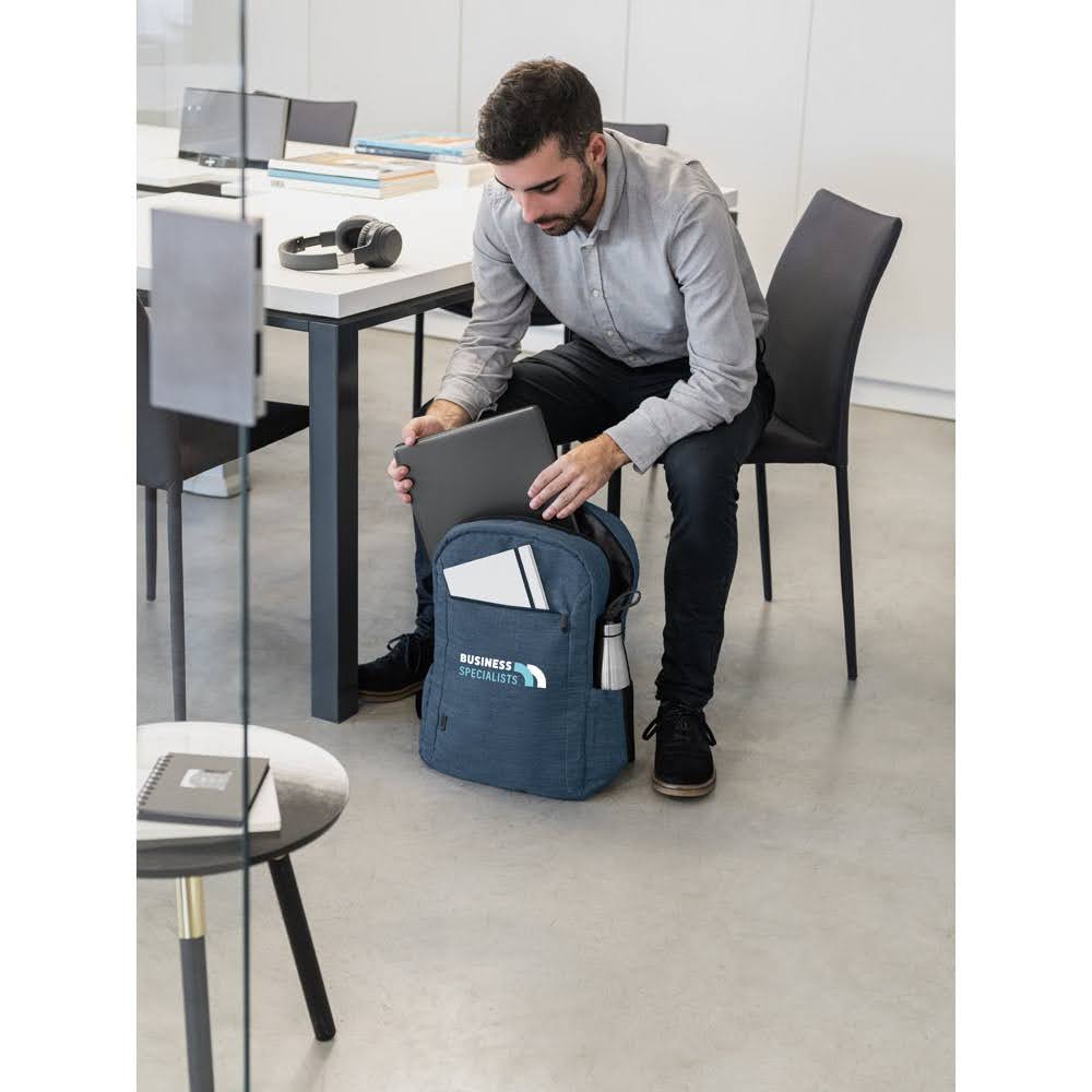 Homem guardando um notebook dentro de uma mochila azul, num escritório